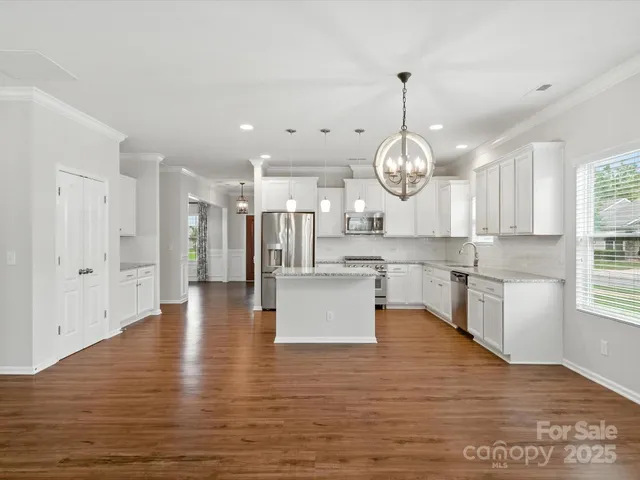 a large kitchen with stainless steel appliances granite countertop a large kitchen island a refrigerator a stove a sink and a wooden floors