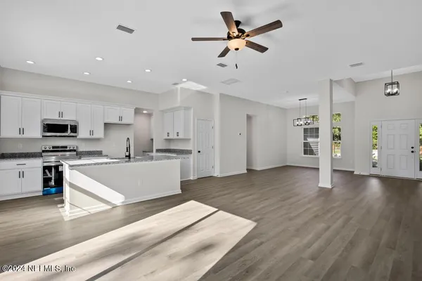 a large kitchen with granite countertop a stove a sink a refrigerator a window and white cabinets