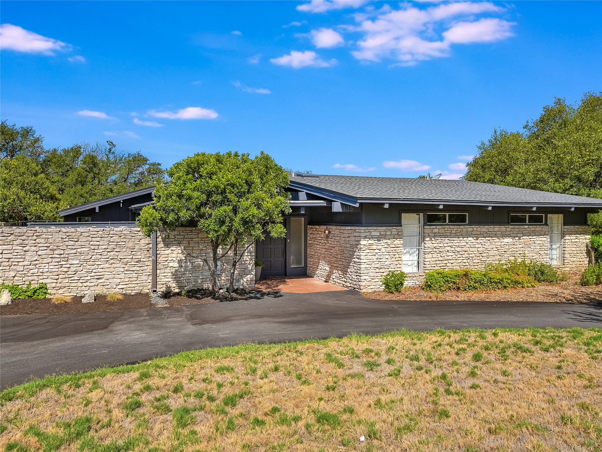 115 Snapper Street Lakeway, TX 78734 - Photo 1 of 30 A striking modern ranch home presents a unique stone and dark facade with a welcoming paved entry.