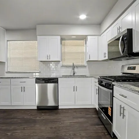 a kitchen with stainless steel appliances white cabinets granite counter tops and a window