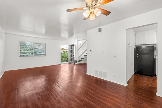 a view of an empty room with wooden floor and a ceiling fan