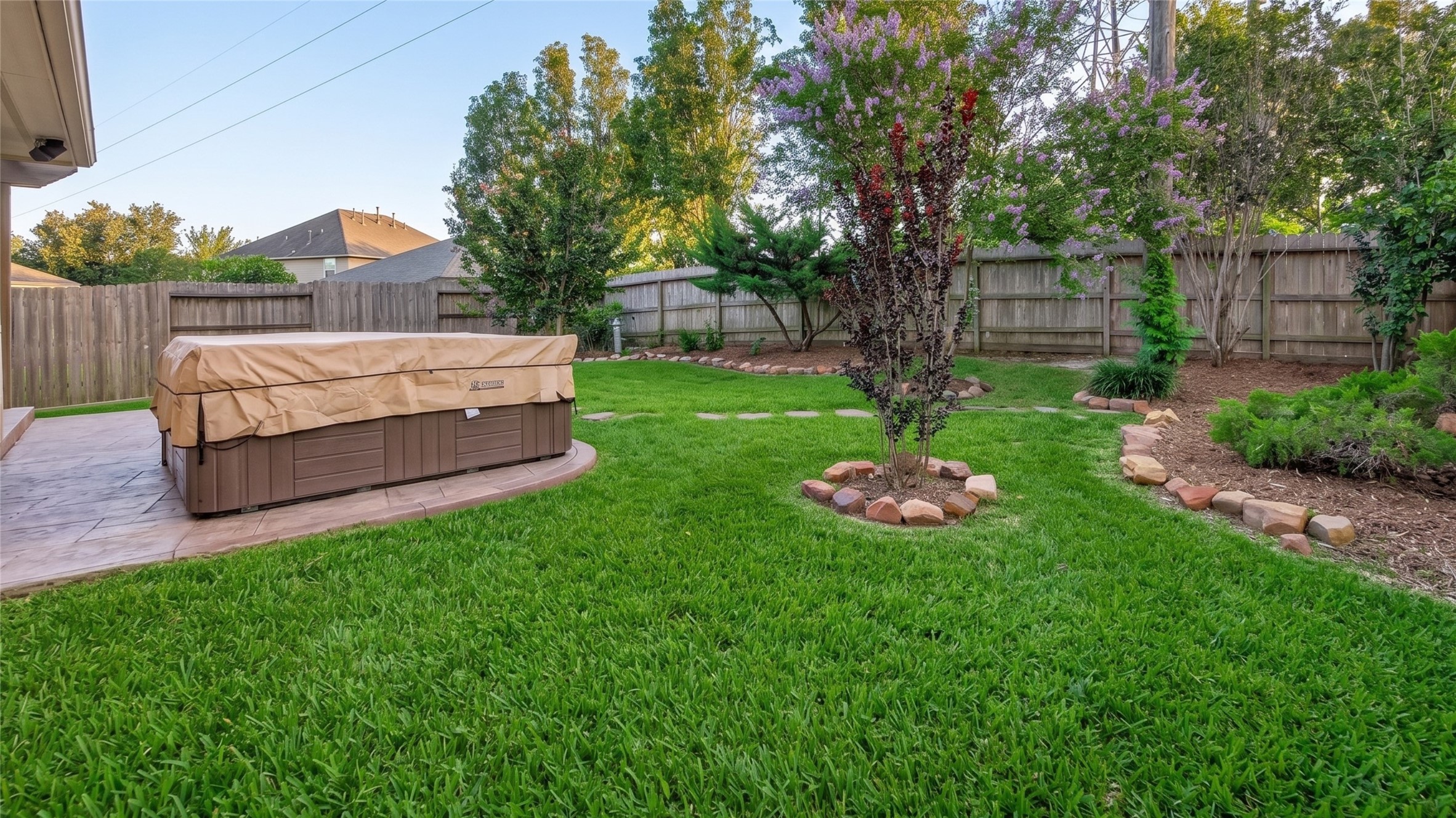 27443 Rebecca Field Lane Spring, TX 77386 - Photo 27 of 31 This backyard features a well-maintained lawn, a covered hot tub on a paved patio, and a variety of trees and shrubs along the wooden fence, offering a private and relaxing outdoor space.