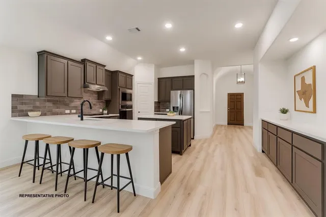 a kitchen with stainless steel appliances granite countertop a refrigerator a sink dishwasher a stove and white cabinets with wooden floor