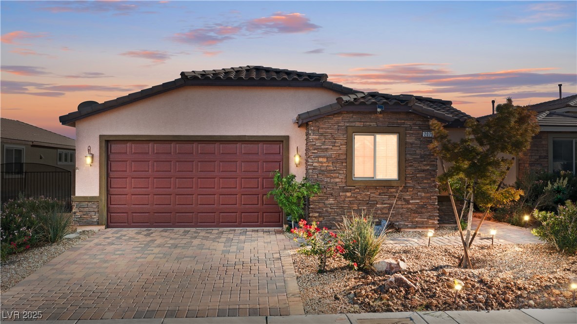 Mediterranean / spanish house with stone siding, stucco siding, decorative driveway, and a garage