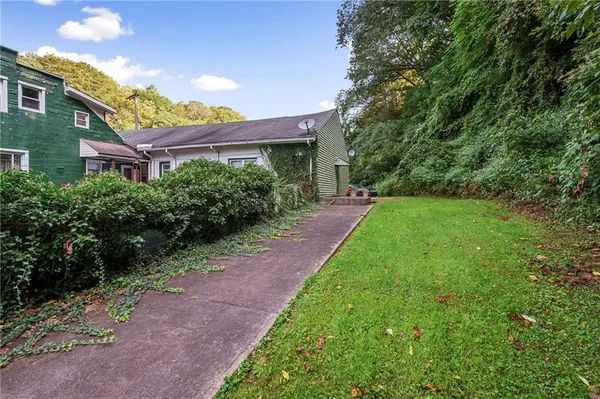 a view of a brick house with a big yard plants and large trees