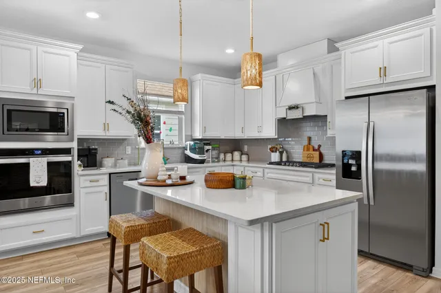 a kitchen with stainless steel appliances a stove a sink a microwave a refrigerator and white cabinets