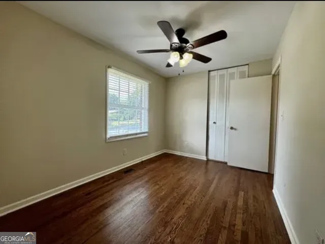 an empty room with wooden floor chandelier fan and windows