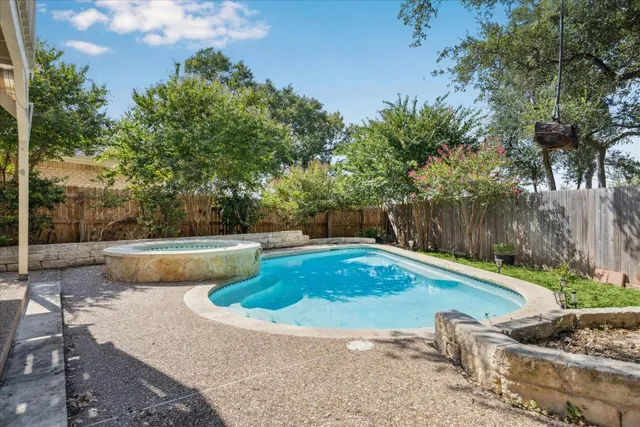 a view of a white house with a large pool and a yard with plants and large trees