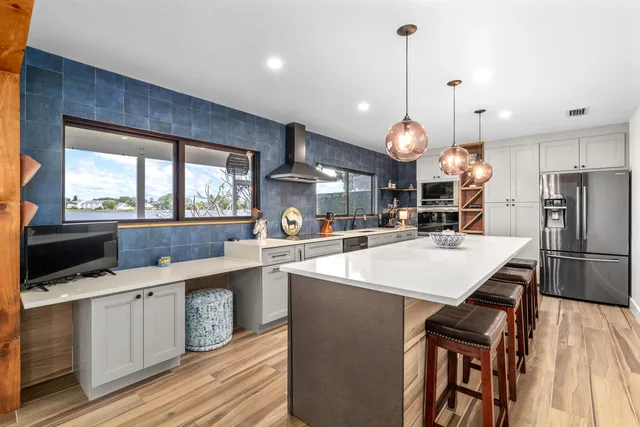 a kitchen with stainless steel appliances a stove a sink a microwave a refrigerator a stove and white cabinets with wooden floor