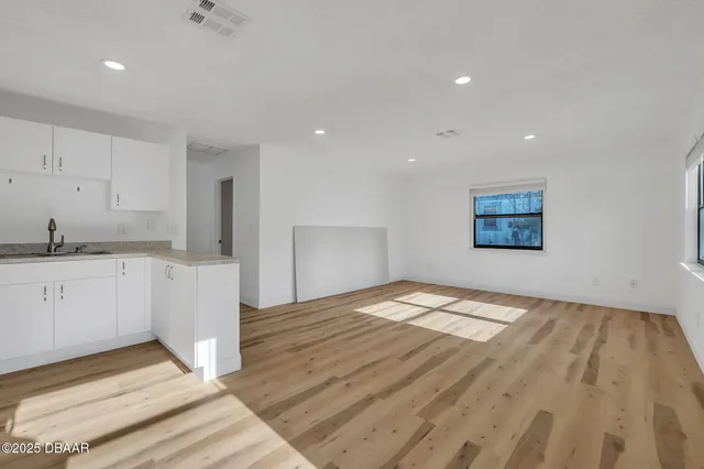 a view of empty room with wooden floor and kitchen