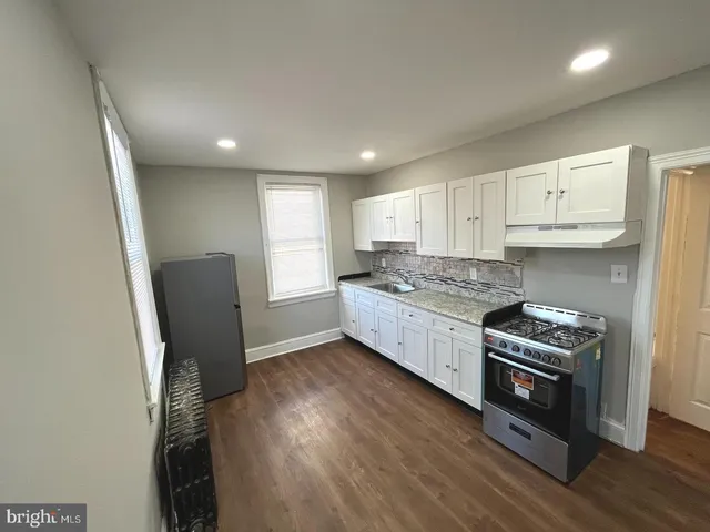 a kitchen with granite countertop a refrigerator a stove a sink and white cabinets