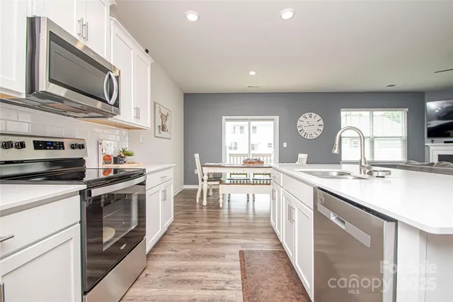 a kitchen with stainless steel appliances granite countertop a stove top oven a sink dishwasher and white cabinets with wooden floor