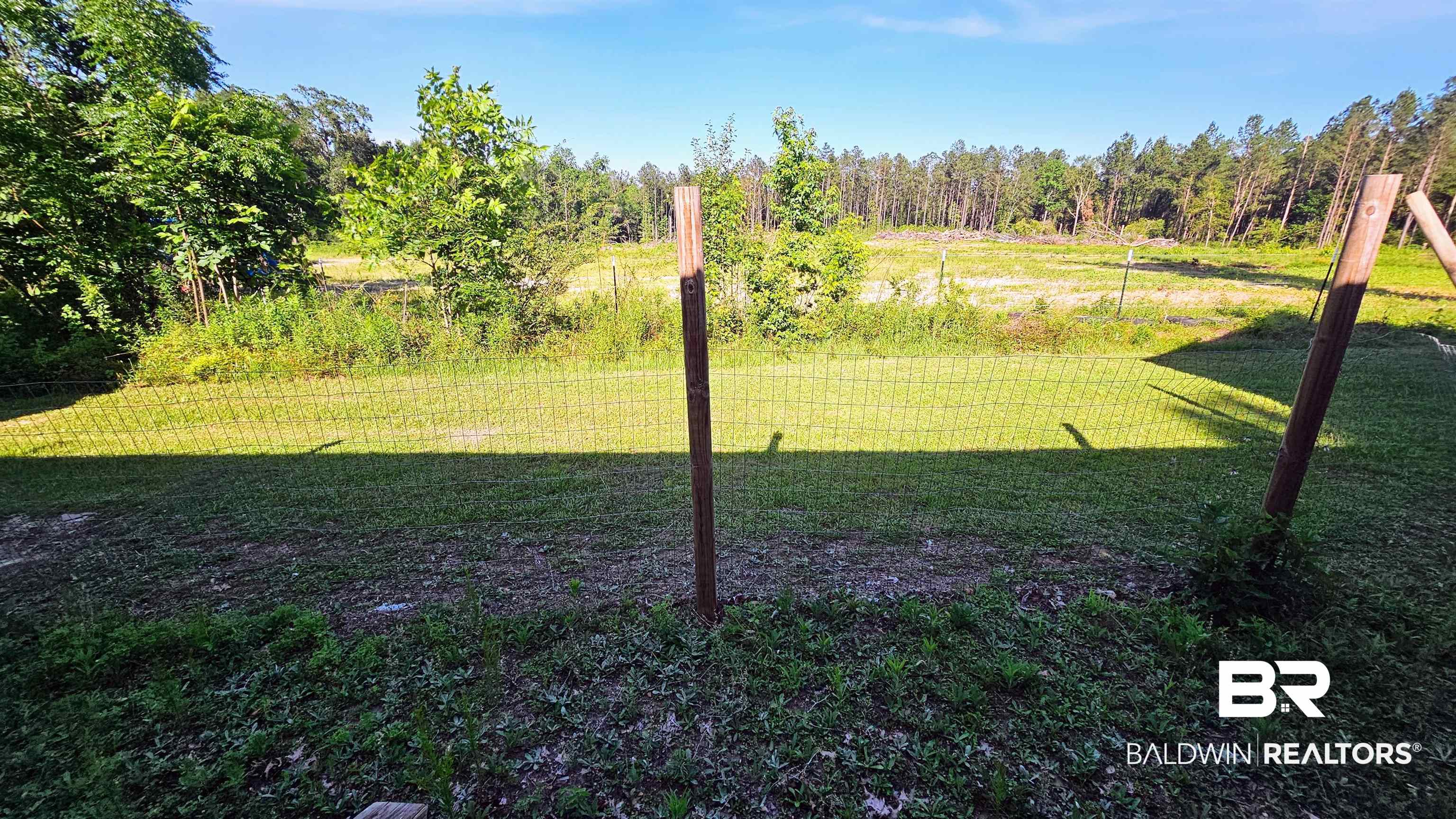 18824 Highway 41 Brewton, AL 36426 - Photo 12 of 40 Grassy yard with wire fencing and wooden posts, bordering a field with dense tree lines