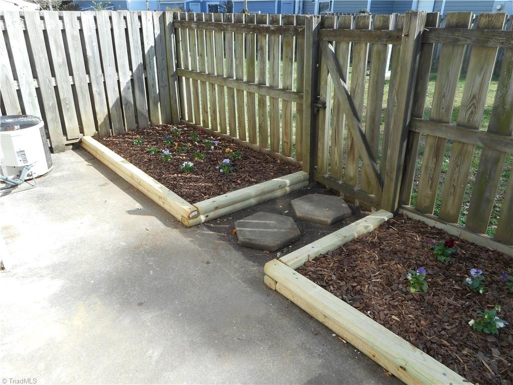 5725 Bramblegate Road, Unit F Greensboro, NC 27409 - Photo 2 of 30 Rear Patio Area: Here we can see part of the paved patio, the privacy fence and the two flower / garden beds for some of your favorite flowers or maybe some vegetables.