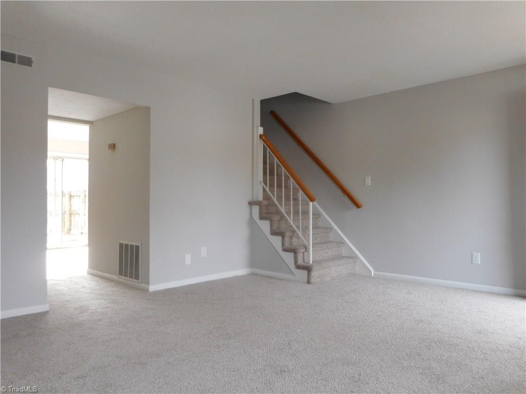 5725 Bramblegate Road, Unit F Greensboro, NC 27409 - Photo 6 of 30 Living Room: Room features include fresh new paint, new carpet flooring and a window for natural lighting. The staircase on the right is to the upper leve. The open doorway shows' the kitchen and dining room.