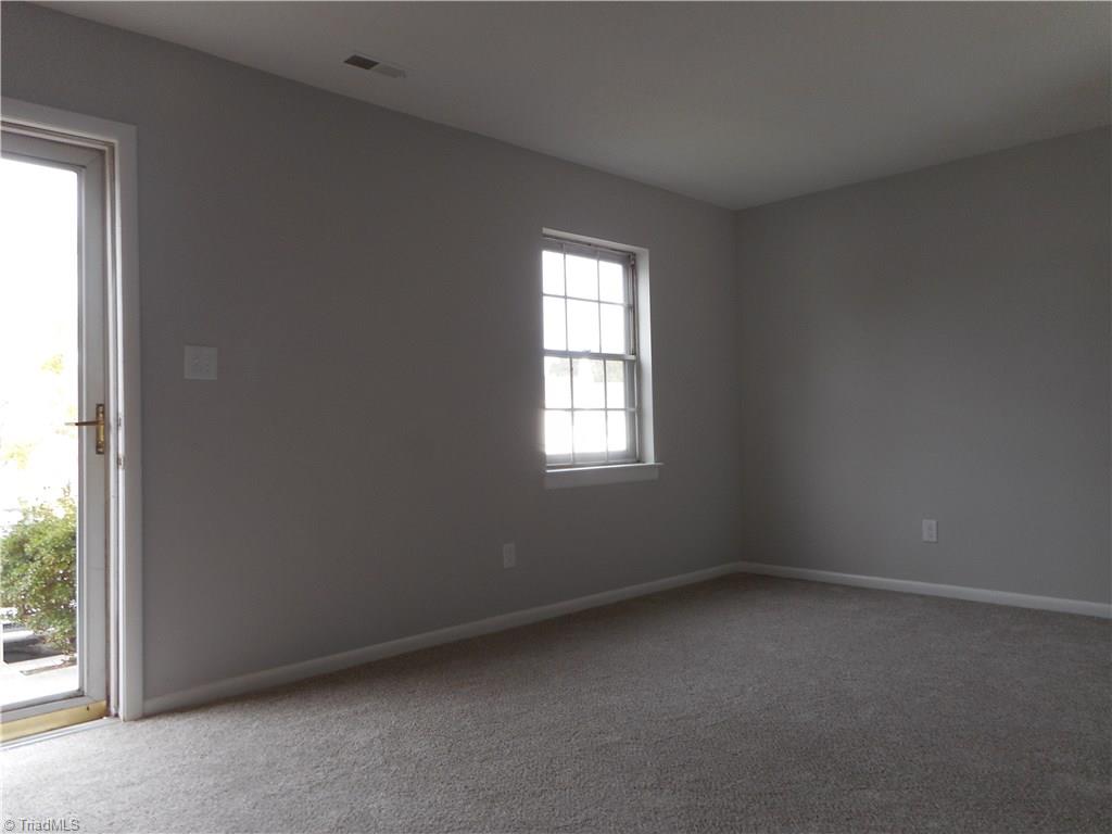 5725 Bramblegate Road, Unit F Greensboro, NC 27409 - Photo 7 of 30 Living Room: Room features include fresh new paint, new carpet flooring and a window for natural lighting. The open doorway shows the front storm door from the front parking lot. To the right side is the kitchen and dining room.