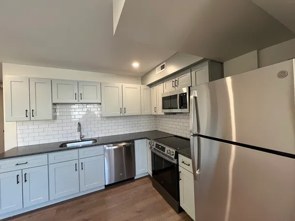 a kitchen with stainless steel appliances granite countertop a refrigerator a sink a stove a microwave and white cabinets