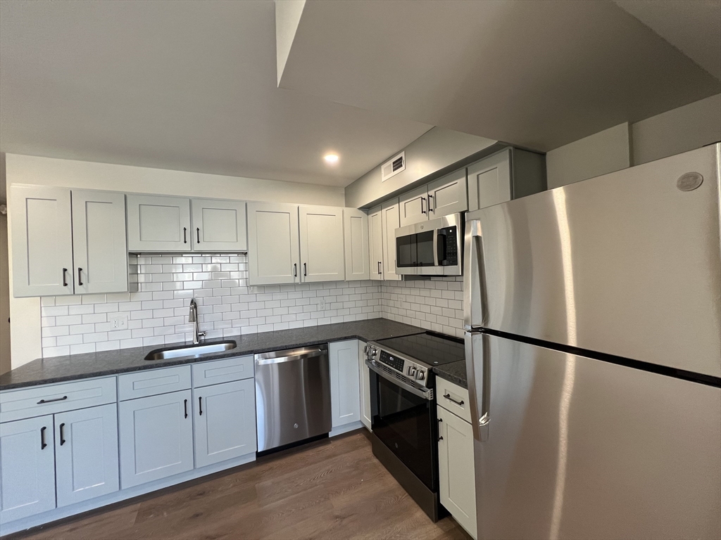 a kitchen with stainless steel appliances granite countertop a refrigerator a sink a stove a microwave and white cabinets