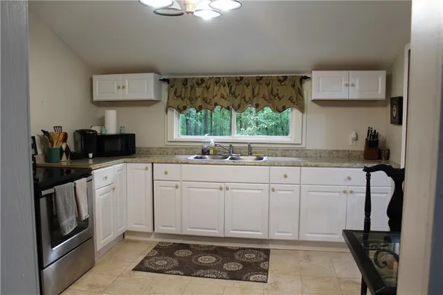 a kitchen with white cabinets a sink a stove and a window