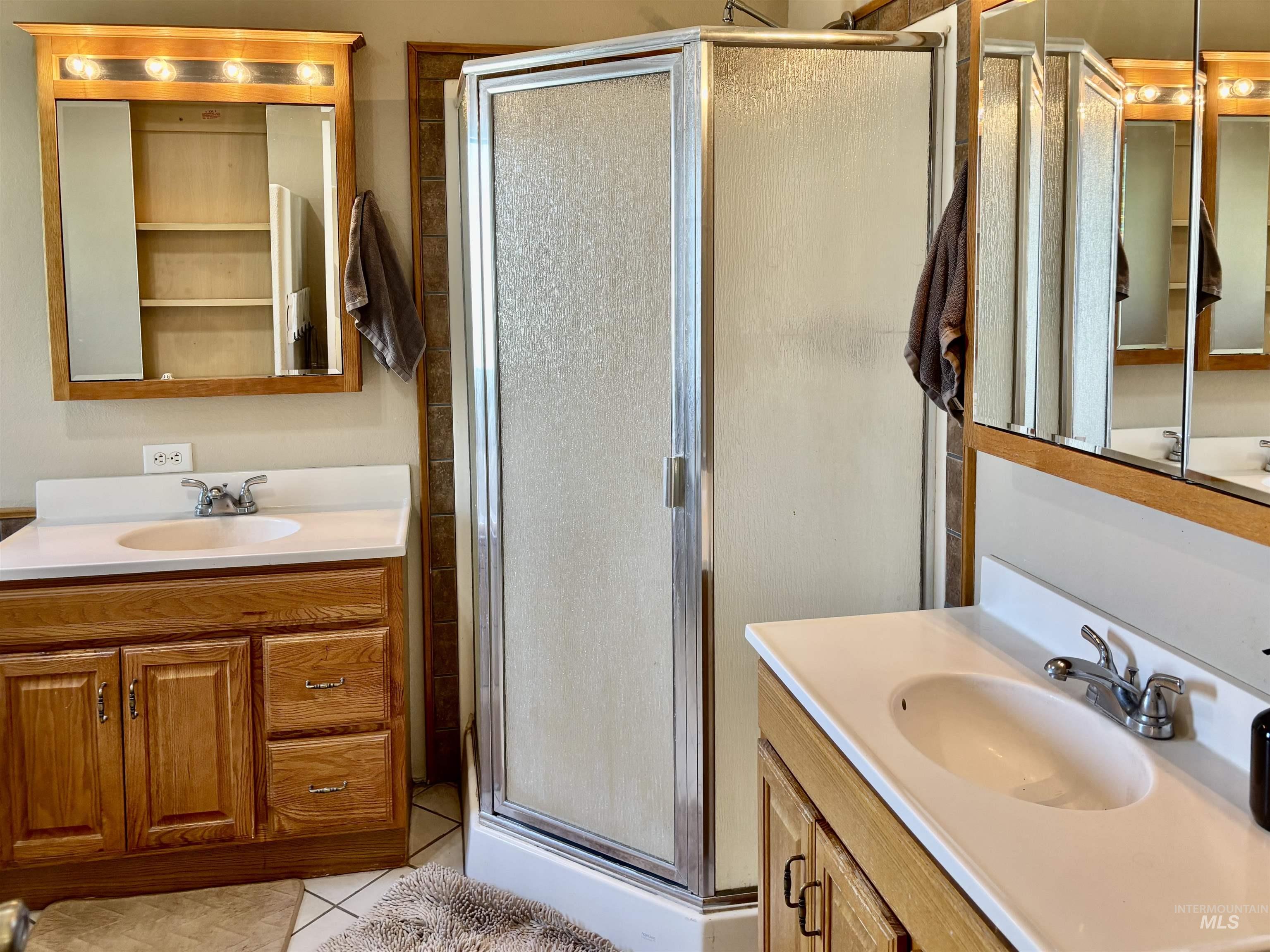 23626 Boise River Road Caldwell, ID 83607 - Photo 21 of 49 Dual wood-finish vanities with integrated sinks and white countertops, individual mirrored medicine cabinets with overhead lighting, and a corner shower enclosure with textured glass