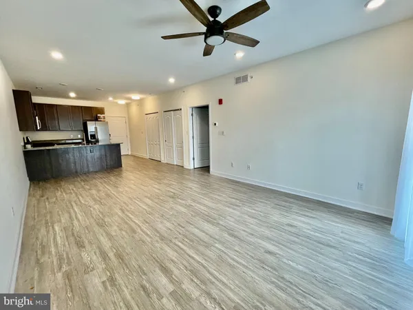 an empty room with wooden floor kitchen view and windows