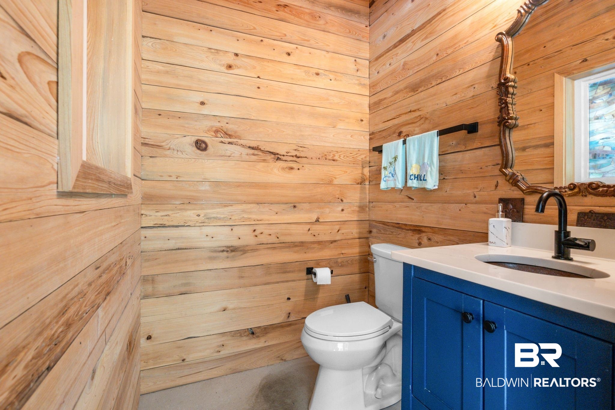 7266 Franklin Road Foley, AL 36535 - Photo 56 of 64 Wood-paneled bathroom featuring a blue vanity with a white countertop and undermount sink, a matte black faucet, and an ornate mirror
