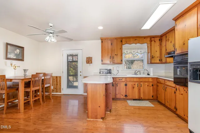 a kitchen with stainless steel appliances granite countertop a refrigerator a stove a sink a dining table and chairs with wooden floor