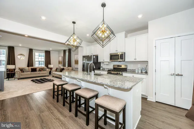 a open kitchen with stainless steel appliances granite countertop a stove a refrigerator a kitchen island a dining table and chairs with wooden floor