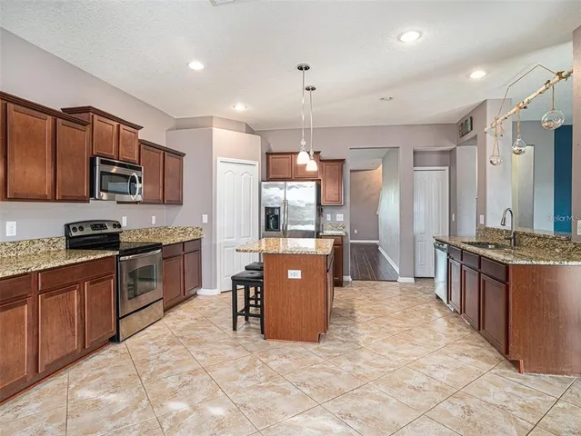 a large kitchen with stainless steel appliances kitchen island granite countertop a stove a sink a refrigerator a microwave oven and a dining table