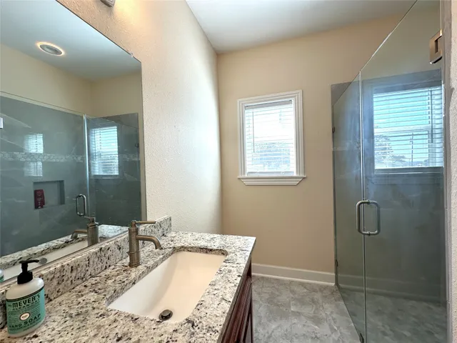 a bathroom with a granite countertop sink a mirror and shower