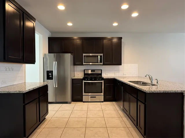 a kitchen with stainless steel appliances granite countertop a refrigerator a sink a stove top oven and cabinets