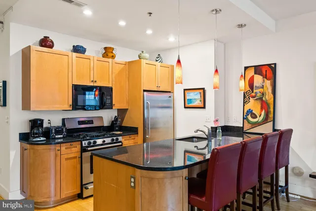 a kitchen with stainless steel appliances granite countertop a stove a refrigerator a microwave a dining table and chairs with wooden floor