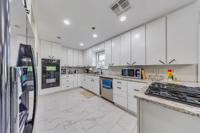 a kitchen with stainless steel appliances granite countertop a refrigerator oven a sink and white cabinets with wooden floor