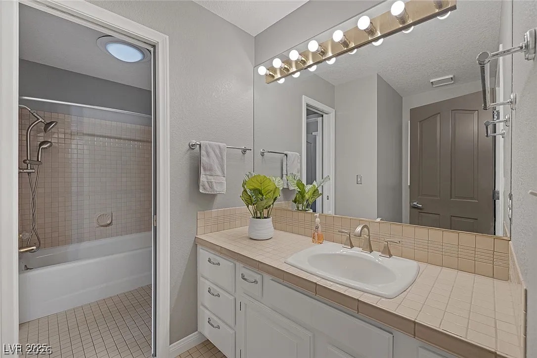 9 Quail Run Road Henderson, NV 89014 - Photo 32 of 57 A pristine bathroom features a tiled vanity, integrated sink, and a shower-tub combination, ready for everyday use.