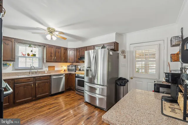 a kitchen with stainless steel appliances granite countertop a refrigerator a sink dishwasher a stove and white countertops with wooden floor