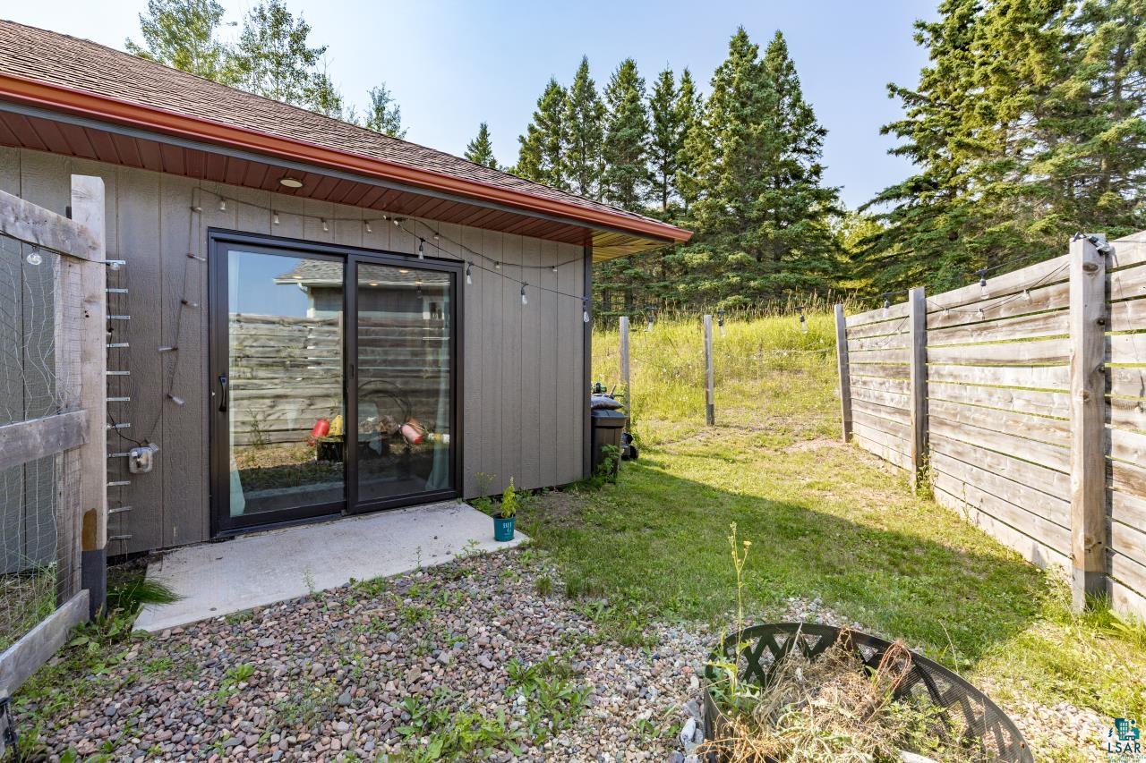 265 Mink Ranch Road Lutsen, MN 55612 - Photo 12 of 33 Siding exterior with a sliding glass door, concrete patio, a wood fence, and surrounding natural foliage