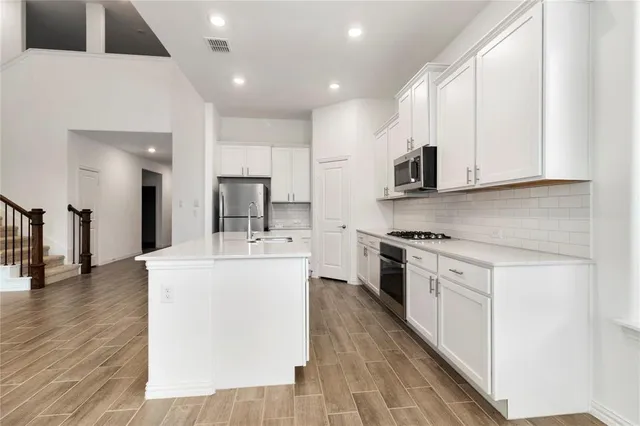 a large kitchen with stainless steel appliances granite countertop a stove a sink and white cabinets with wooden floor