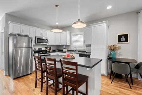 a kitchen with stainless steel appliances granite countertop a refrigerator a stove a sink a dining table and chairs with wooden floor