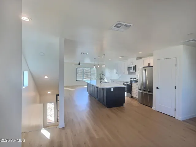 a kitchen with stainless steel appliances kitchen island granite countertop a refrigerator a sink a stove and a microwave with wooden floor