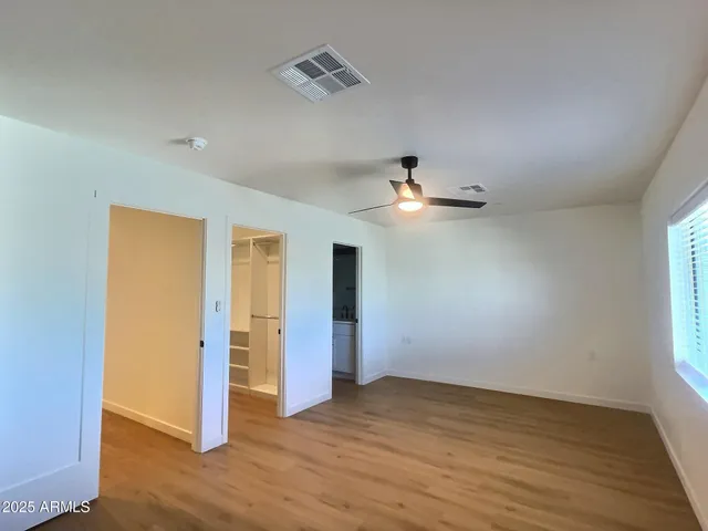 an empty room with wooden floor chandelier fan and windows