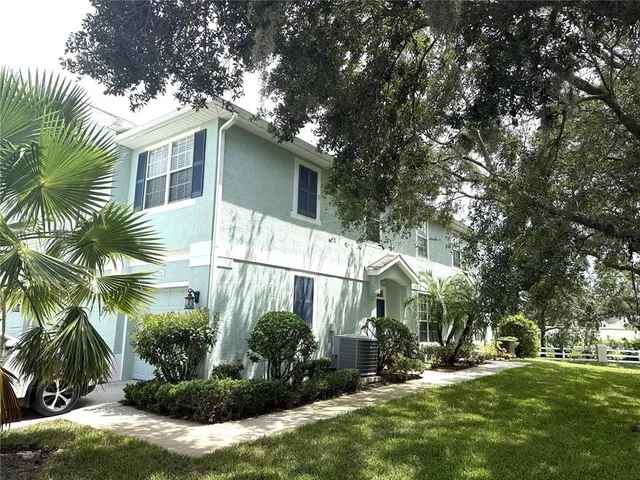 a view of a white house with a big yard and potted plants and large trees