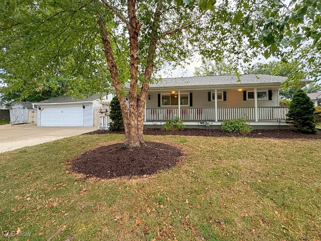 Single story home featuring a garage, a front yard, covered porch, and an outbuilding