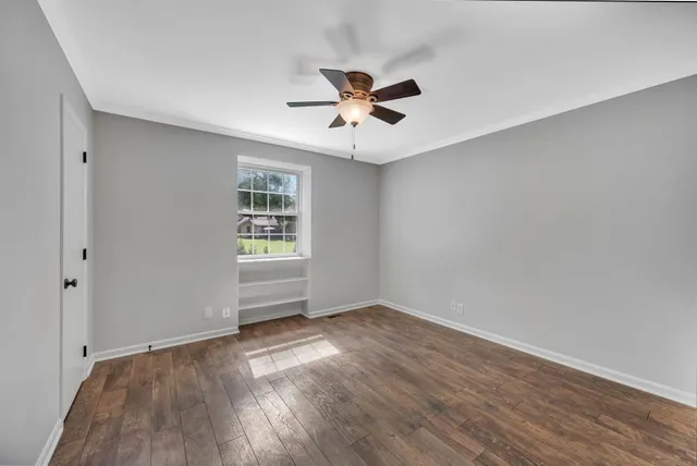 an empty room with wooden floor ceiling fan and windows