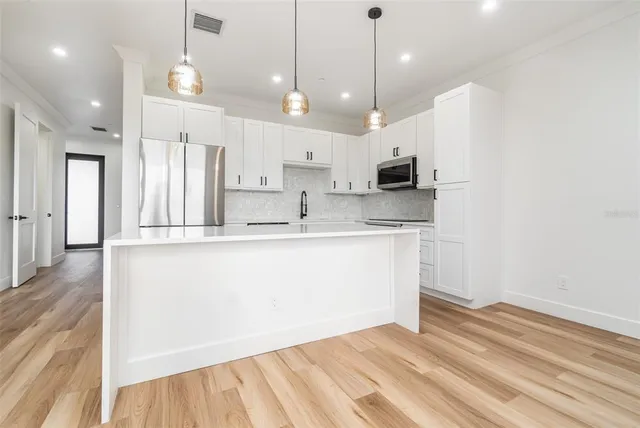 a kitchen with kitchen island a stove a refrigerator a sink and white cabinets with wooden floor