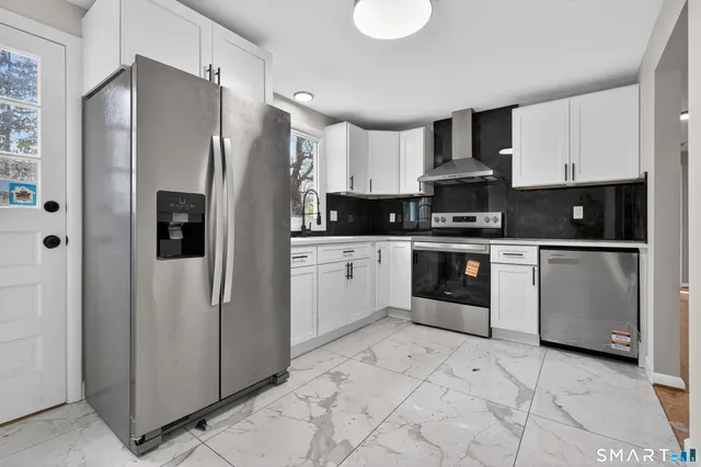 a kitchen with stainless steel appliances granite countertop a refrigerator a stove a sink and white cabinets