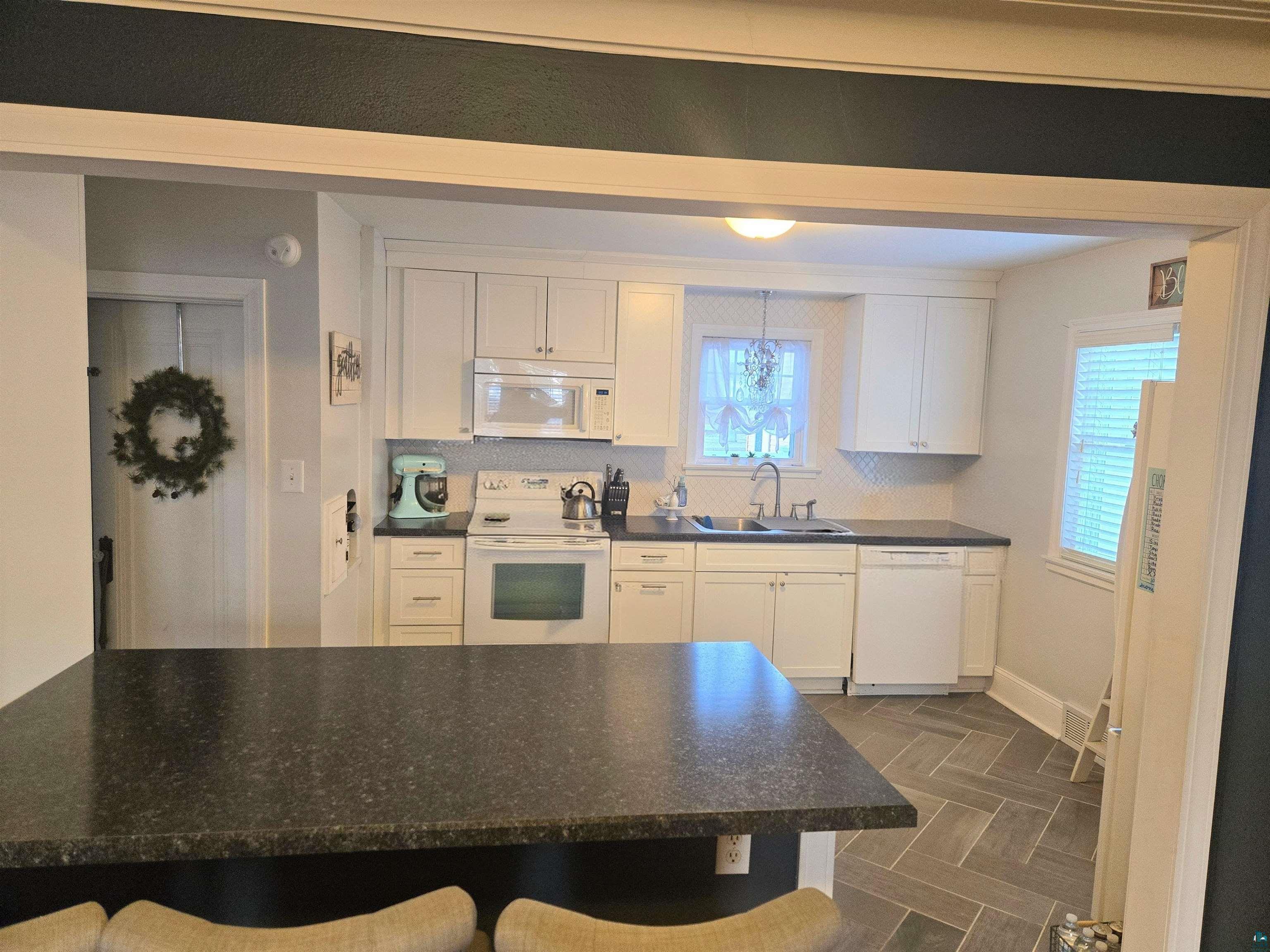 4327 West 5th Street Duluth, MN 55807 - Photo 11 of 25 Kitchen with white appliances, dark countertops, white cabinets, and a kitchen breakfast bar