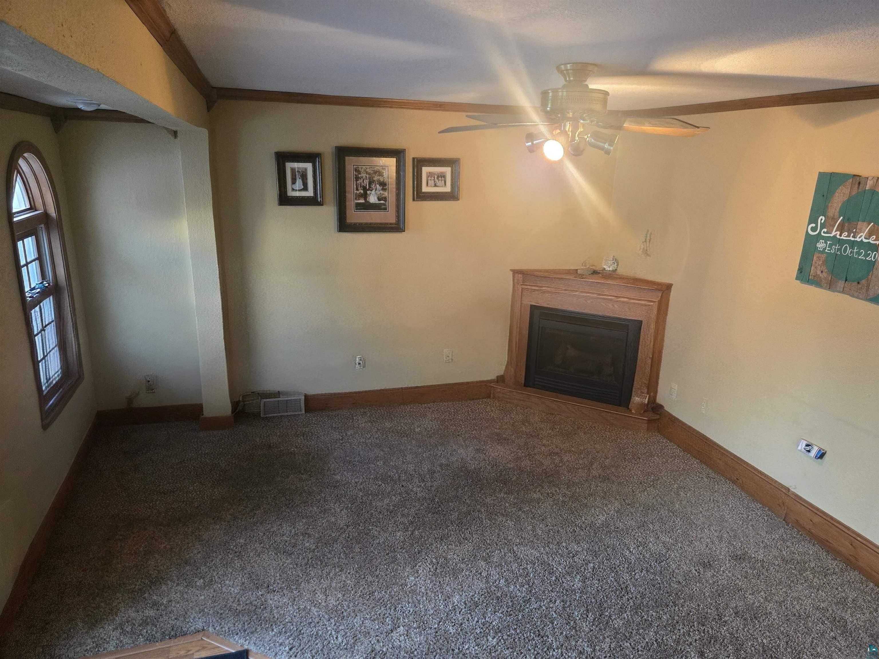 4327 West 5th Street Duluth, MN 55807 - Photo 14 of 25 Unfurnished living room with carpet flooring, ceiling fan, ornamental molding, and a glass covered fireplace