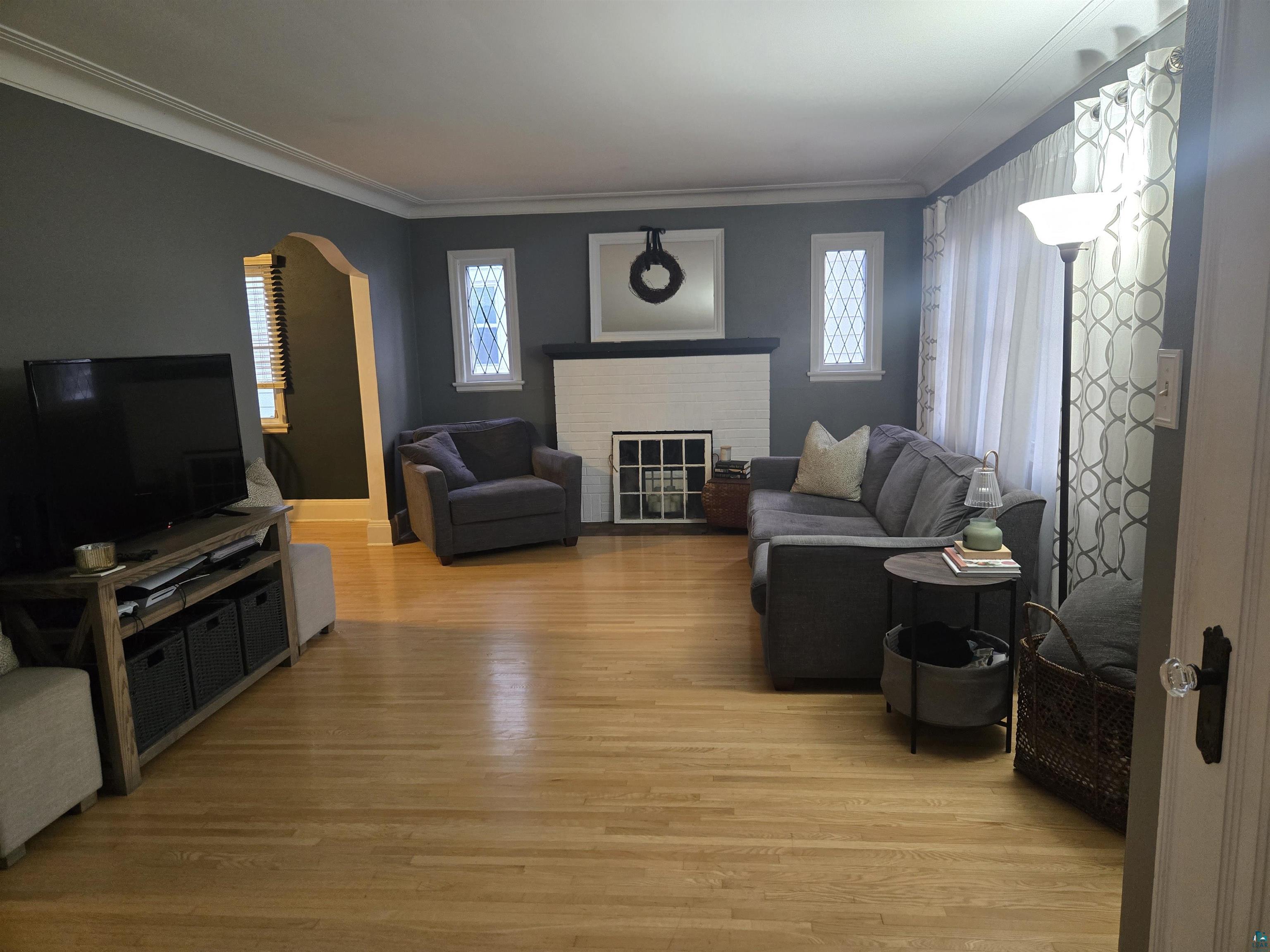 4327 West 5th Street Duluth, MN 55807 - Photo 5 of 25 Living room featuring light wood finished floors, arched walkways, a brick fireplace, plenty of natural light, and ornamental molding