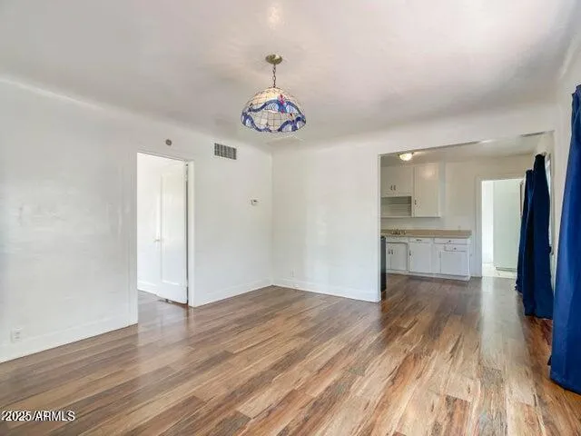 a view of an empty room with wooden floor and a kitchen