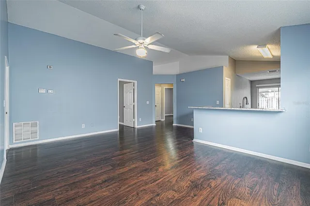 a view of an empty room with wooden floor and a ceiling fan